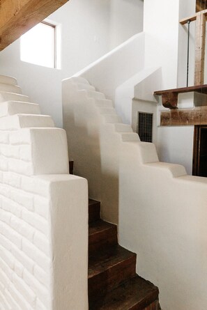 Eine Treppe mit weißen Stufen und hölzernen Geländern, die zu einer Zwischenebene mit einem Balkenwerk führt.