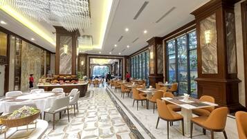Un vaste espace de restauration d’hôtel, doté d’un sol en marbre, de lustres modernes et d’un long comptoir où sont présentés les plats.