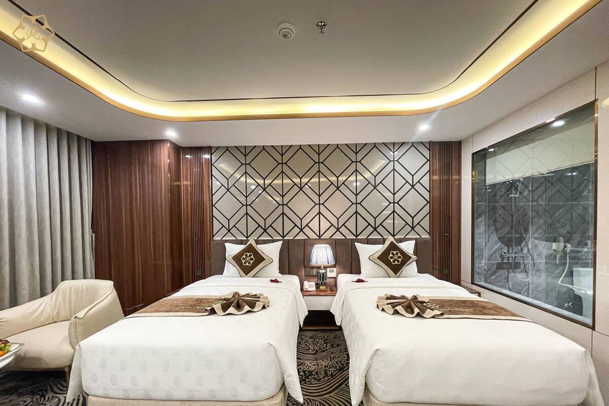 Une chambre d’hôtel avec deux lits, un bureau avec une lampe, une chaise et une grande fenêtre.