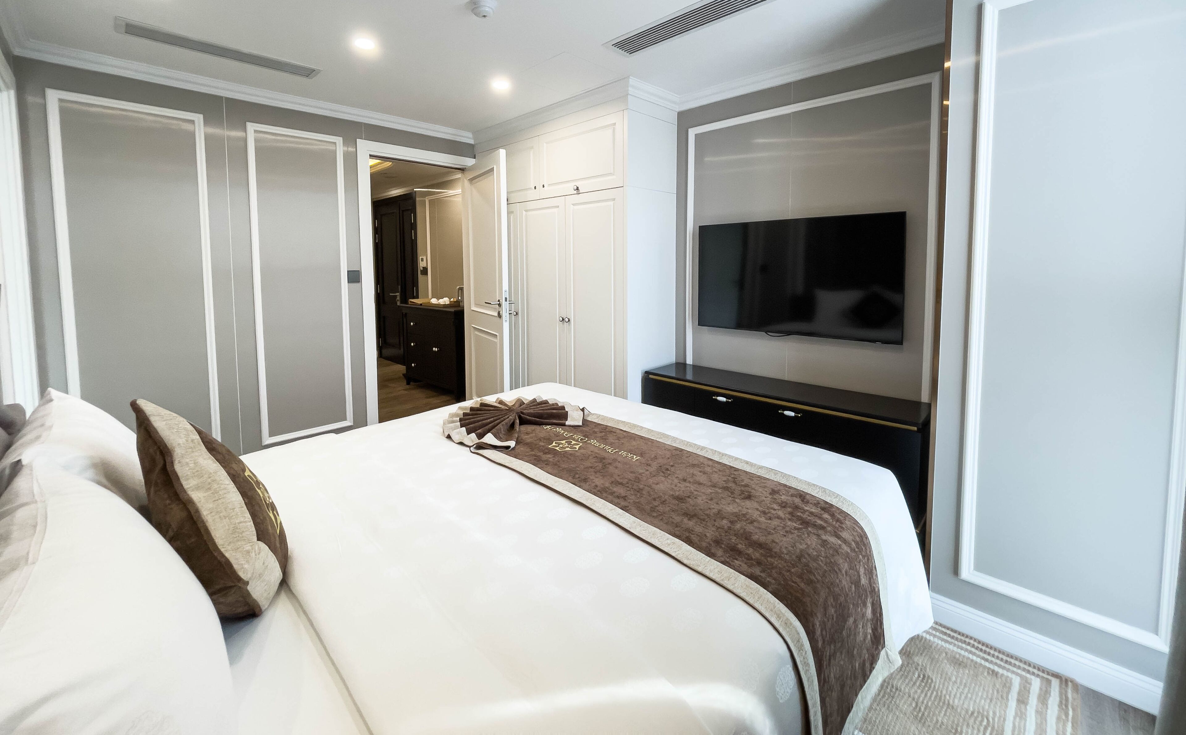 A hotel room with a bed, a TV mounted on the wall, and a wardrobe.