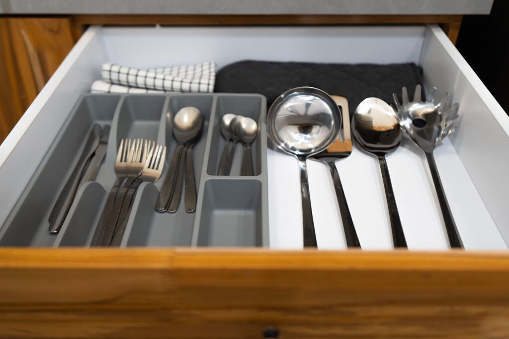 A drawer with utensils neatly organized, including forks, spoons, and a mixing bowl.