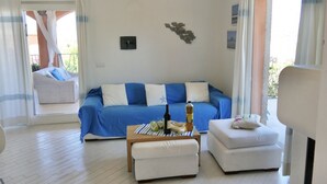 A modern living room with a blue sofa, white cushions, a wooden coffee table with a bottle and glasses, and a small white ottoman. - Villa Ursula, 10 beds, 4 bedrooms, 4 bathrooms, sea view (San Teodoro)