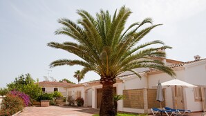 A courtyard with a palm tree, a white building with a tiled roof, and a covered seating area with blue lounge chairs. - LLAMPUDOL (VILLA SA COMA) - Wonderful villa with private pool and free WiFi. (Sant Llorenç des Cardassar)
