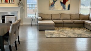 A spacious living room with a large sectional sofa, a dining table with chairs, a fireplace, and a large abstract painting. - 2026 Virginia Tech Graduation Home with Mountain Views ~4 miles to VT (Blacksburg)