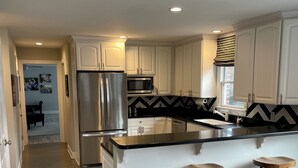 A modern kitchen with white cabinets, stainless steel appliances, a black and white backsplash, and a central island with stools. - 2026 Virginia Tech Graduation Home with Mountain Views ~4 miles to VT (Blacksburg)