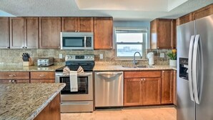 A modern kitchen with wooden cabinets, stainless steel appliances, granite countertops, and a city view through the window.