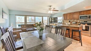 A spacious dining area with a wooden table and chairs, a ceiling fan, and a kitchen with wooden cabinets and a microwave.