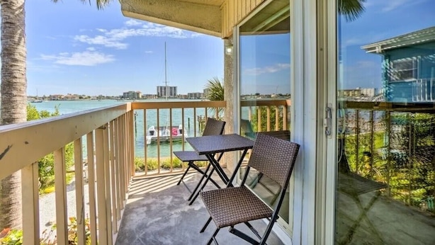 A balcony with a view of the sea, two wicker chairs, and a glass door.