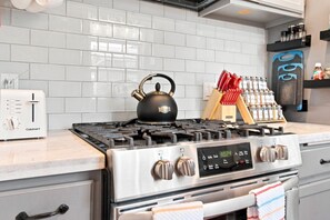 Una cocina con un tostador Cuisinart, un hervidor negro, una estufa a gas con controles de acero inoxidable y un especiero con frascos.