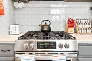 Una cocina con estufa a gas, un reloj digital, un tostador y un especiero.