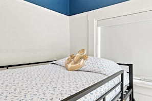 A single bed with a patterned bedspread and a decorative pillow, a white wall, and a blue ceiling.