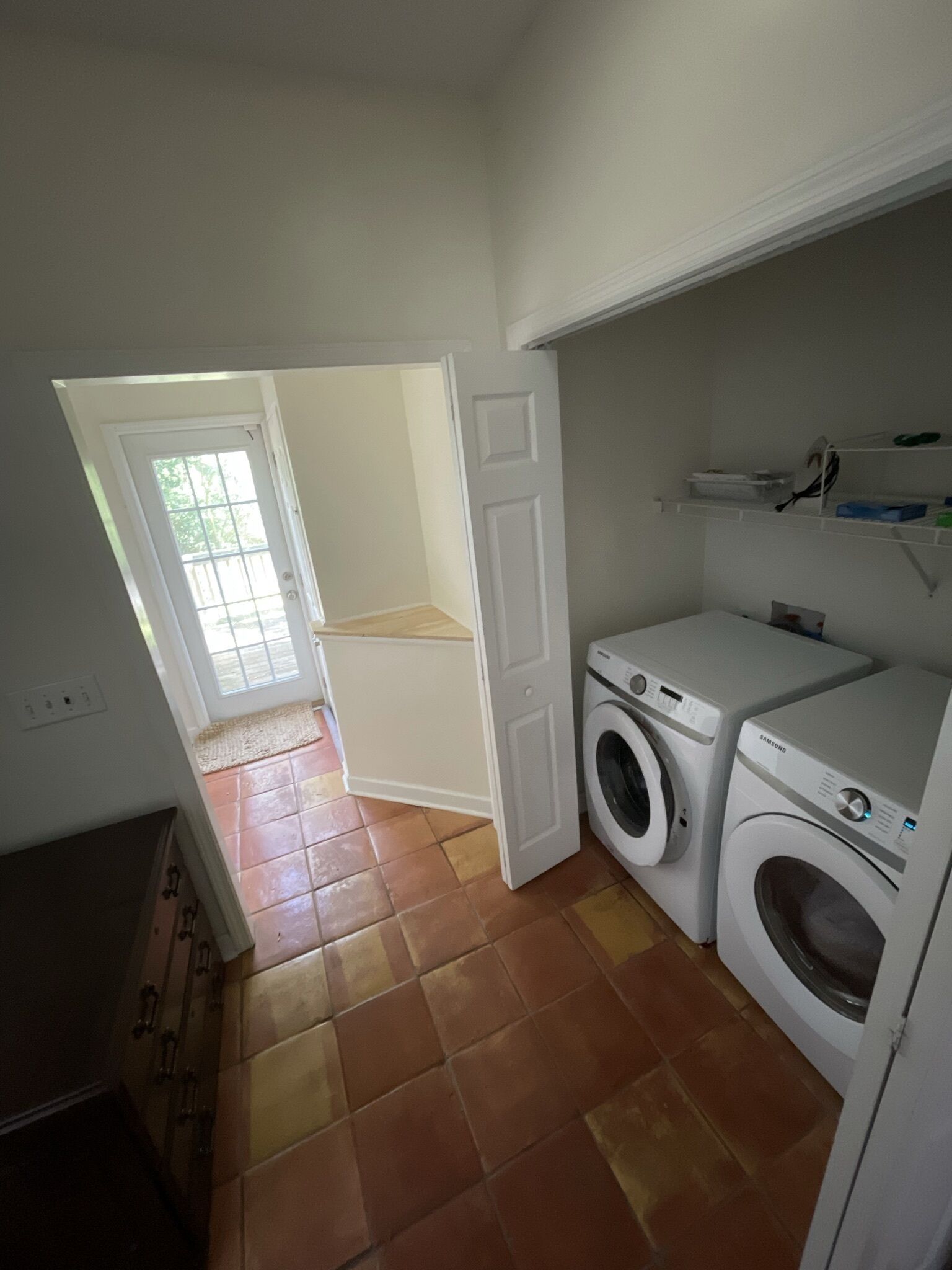 A laundry room with two washing machines, a white door, and a tiled floor.