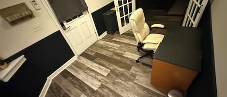 Una habitación con piso de madera, una puerta blanca, un cortinaje negro, una silla blanca y una pequeña mesa con tapa negra.