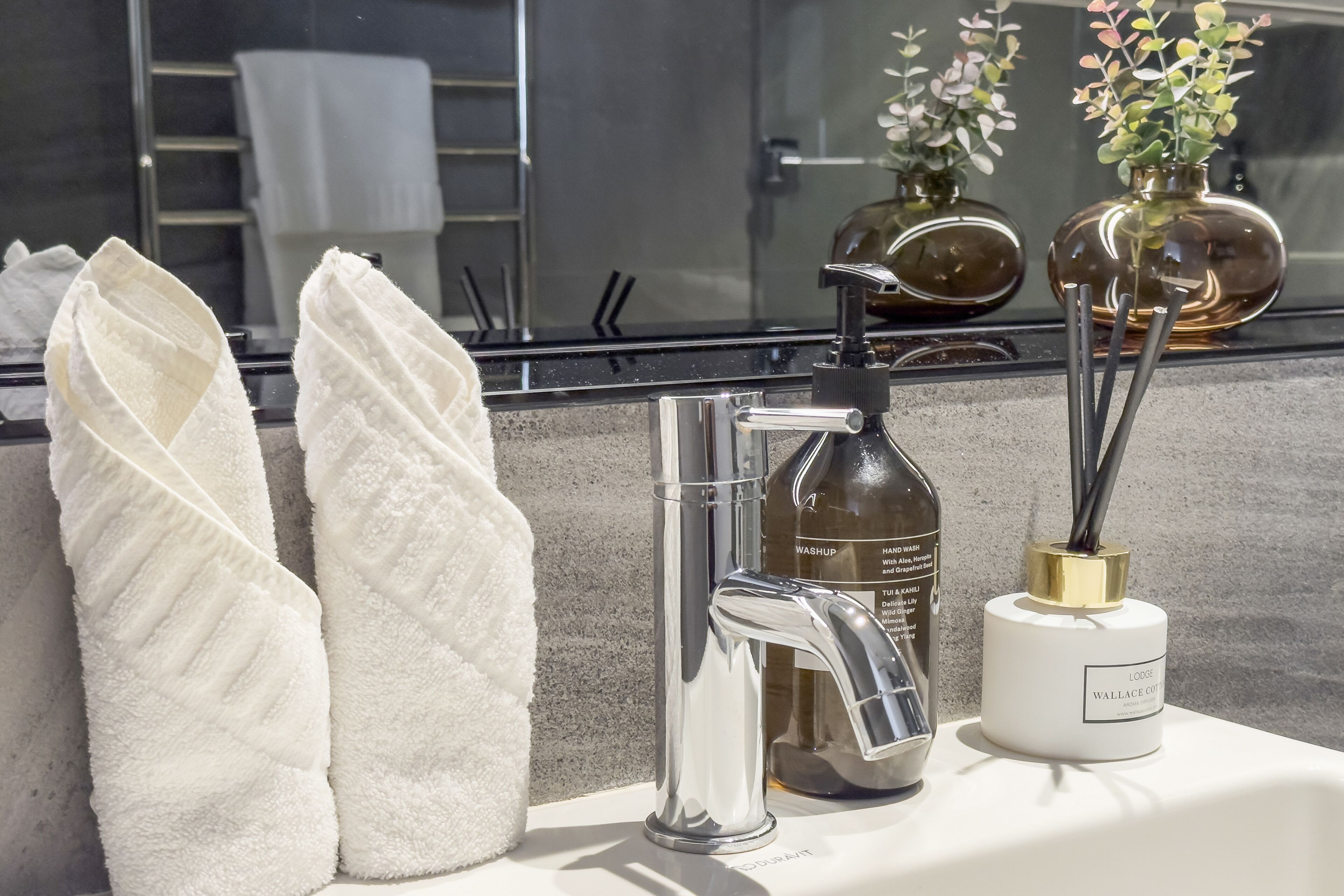 A bathroom with a modern sink, a hand soap dispenser, and a vase with a plant.