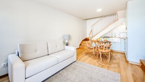 En moderne stue med sofa, spisebord med stole og trappe op til et køkken.