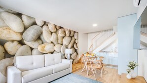 Ein modernes Wohnzimmer mit Steinwand, einem weißen Sofa, einem Esstisch mit Stühlen und einer Treppe.