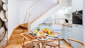 Eine moderne Küche mit einer Holztreppe, weißen Schränken und einer Frühstücksvorbereitung mit Croissants, Saft und einem Blumenstrauß.
