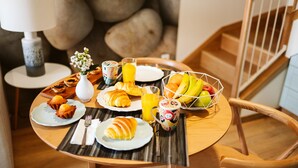 Ein Frühstückstisch mit Croissants, Muffins, einer Obstschale und einem Fruchtsaft.