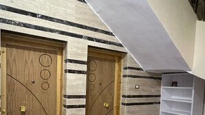 Un couloir avec deux portes en bois, une étagère blanche et des carreaux de sol à motifs.