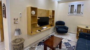 Una sala de estar moderna con un televisor de pantalla plana, un sofá azul, un tapete estampado y una lámpara decorativa.