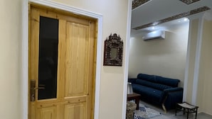 Un salón espacioso con una puerta de madera, un sofá azul y una alfombra estampada.