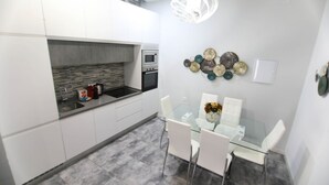 A modern kitchen with white cabinets, a glass dining table, and a unique wall decoration. - RentalSevilla 3 bedroom apartment in Triana (Sevilla)