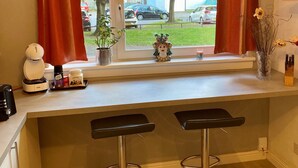 A kitchen with a window view, a coffee machine, a plant, and two bar stools. - Apartment Sleeps 5 with Free Parking (Edinburgh)