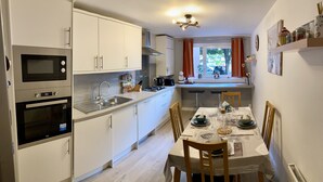 A modern kitchen with white cabinets, a built-in oven, and a gas stove. There is a dining table set with plates and glasses. - Apartment Sleeps 5 with Free Parking (Edinburgh)