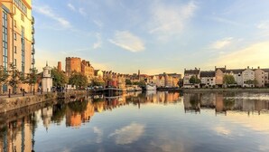 A river with buildings on both sides, including a castle-like structure and modern buildings. - Apartment Sleeps 5 with Free Parking (Edinburgh)