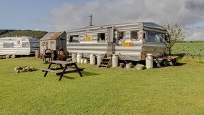 A vintage RV with a small attached structure, a picnic table, and several storage bins in a grassy field. - 2 x Double Bed Glamping Wagon at Dalby Forest (Scarborough)