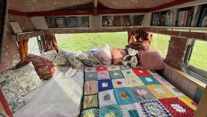 A cozy interior with a bed, pillows, a quilt, a window with a view, and a bookshelf with books. - 2 x Double Bed Glamping Wagon at Dalby Forest (Scarborough)