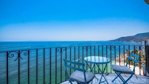 Un balcon avec vue sur la mer et sur le paysage urbain au loin.