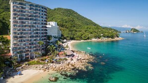 Un hôtel à plusieurs étages doté de balcons, situé près d’une plage et bordant une eau turquoise et cristalline.