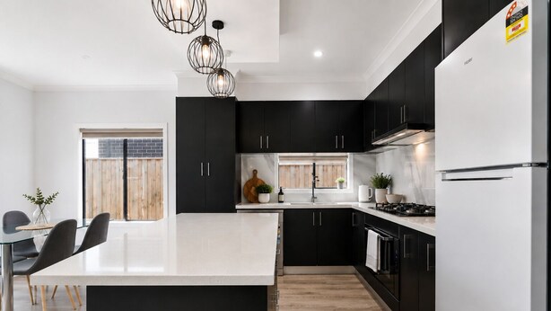 Una cocina moderna con armarios negros, una isla blanca e iluminación colgante.