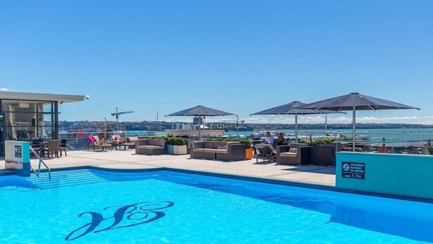 A pool area with lounge chairs and umbrellas, a lifeguard tower, and a view of the sea. - Perfect City Pad (Auckland)