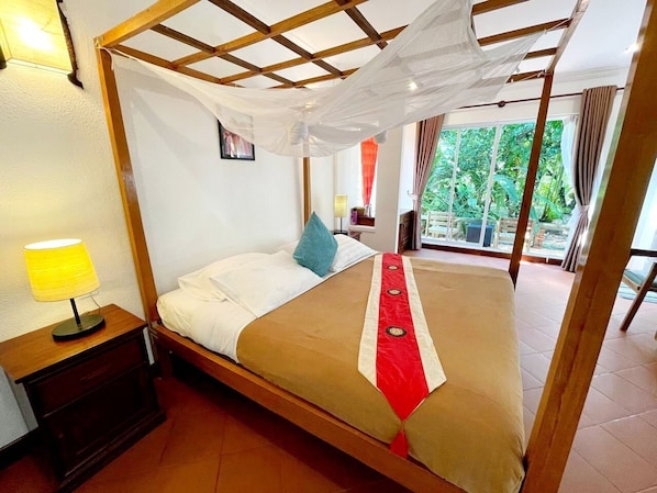 A room with a bed, a nightstand, a lamp, and a view of greenery outside. - Sabbay Kep (Kep)