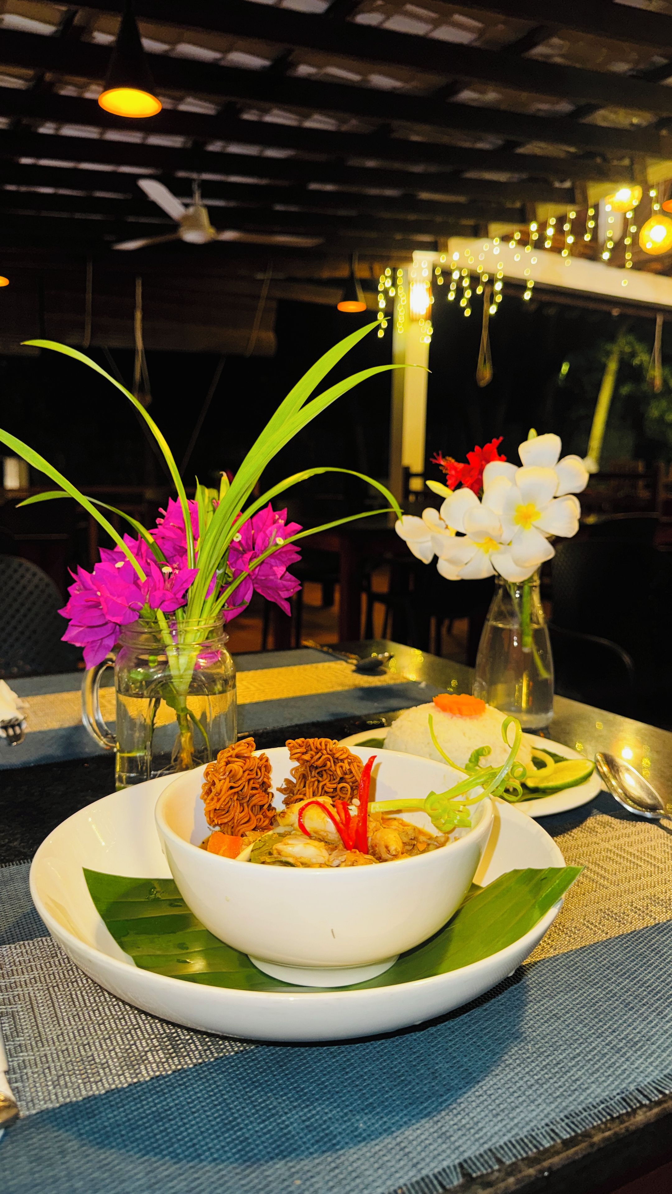 A dining table with a bowl of food, two vases with flowers, and a spoon.
