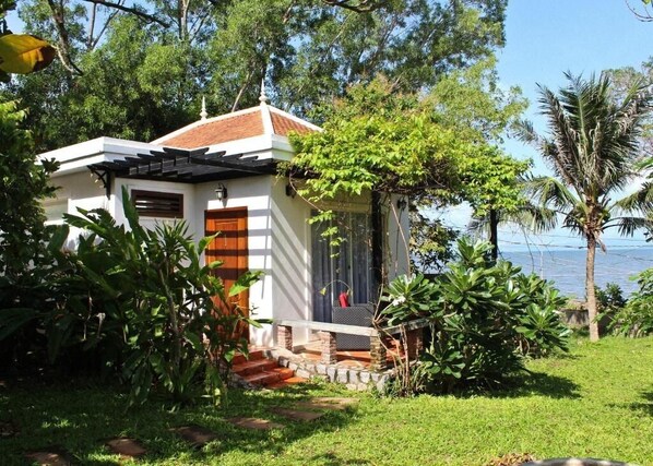 Un petit bâtiment blanc, doté d’un toit en tuiles, entouré d’une végétation luxuriante et d’un palmier.