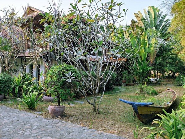 Un jardín con diversas plantas, un bote y una casa con techo de paja.