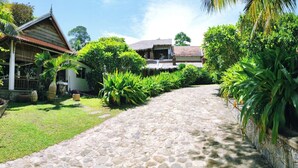 A stone pathway leading to a traditional house with a thatched roof, surrounded by lush greenery. - Sabbay Kep (Kep)