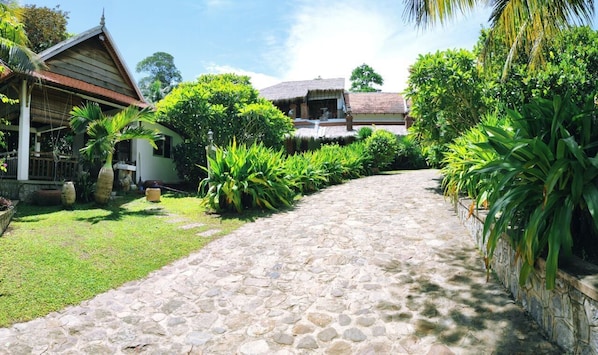 A stone pathway leading to a traditional house with a thatched roof, surrounded by lush greenery. - Sabbay Kep Boutique Resort (Kep)