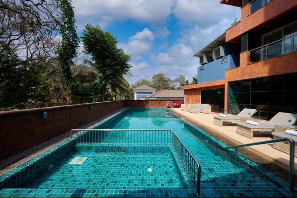 A swimming pool with a tiled floor, surrounded by lounge chairs and a brick wall.
