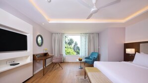 A hotel room with a bed, a desk, a chair, a TV, a window with curtains, and a ceiling fan.