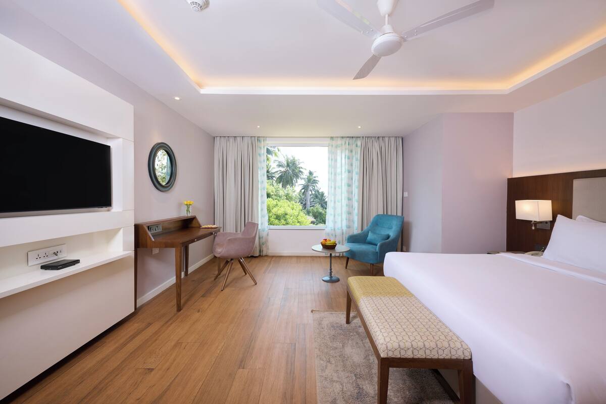 A hotel room with a bed, a desk, a chair, a TV, a window with curtains, and a ceiling fan.