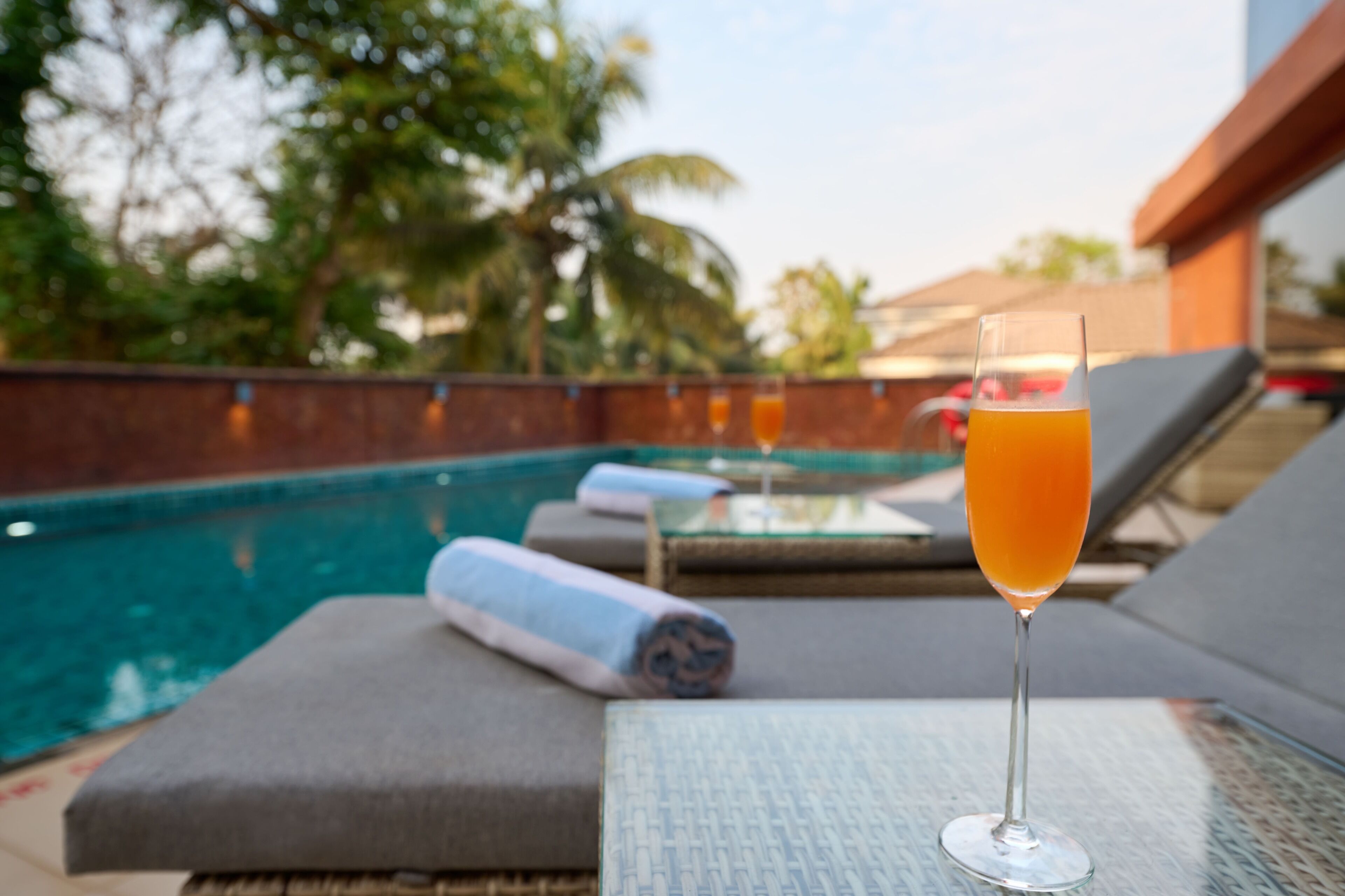 A glass of orange juice on a table with a pool in the background.