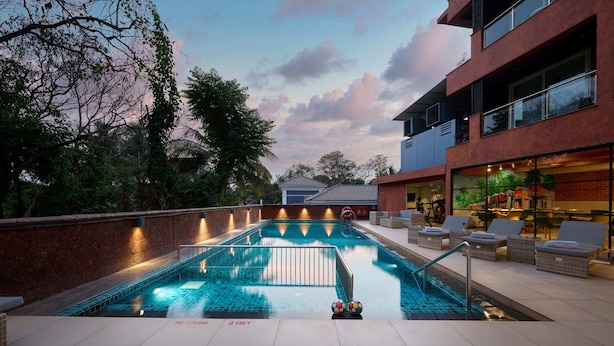 A swimming pool with a tiled deck, lounge chairs, and a view of a building with a balcony.