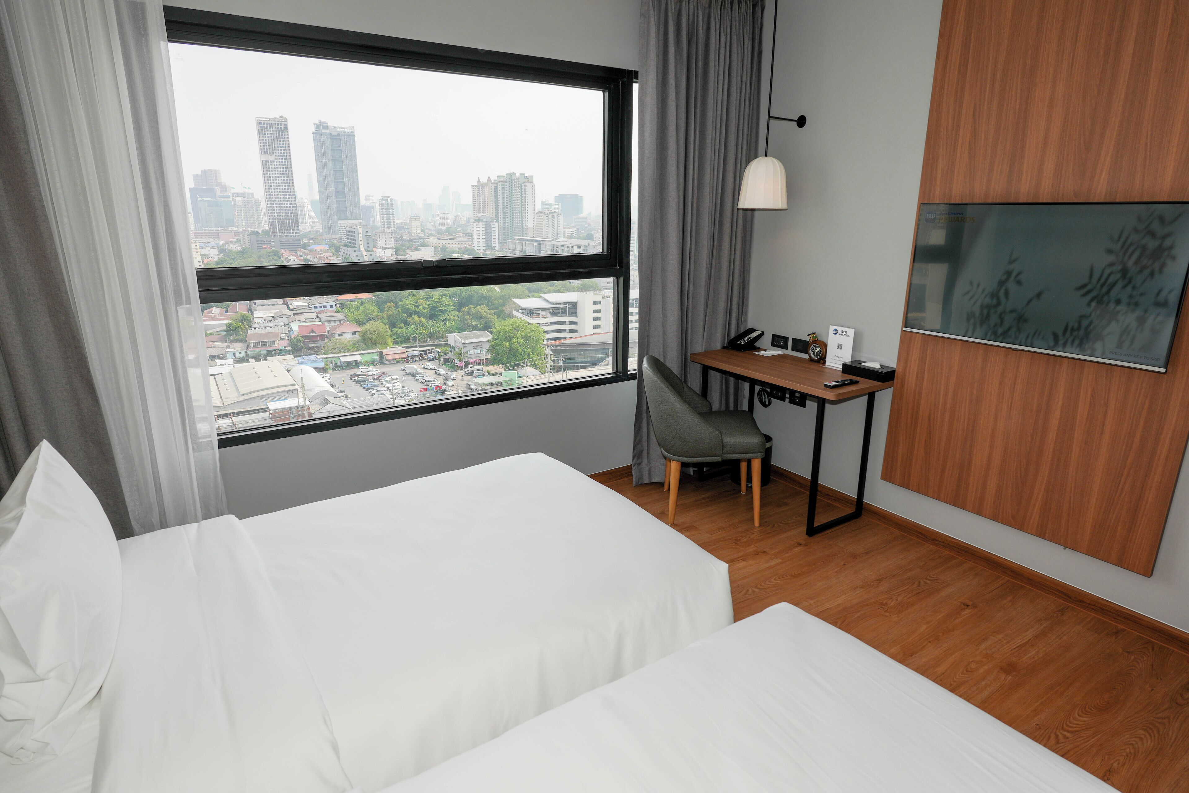 A hotel room with a large window, a bed, a desk, and a chair.