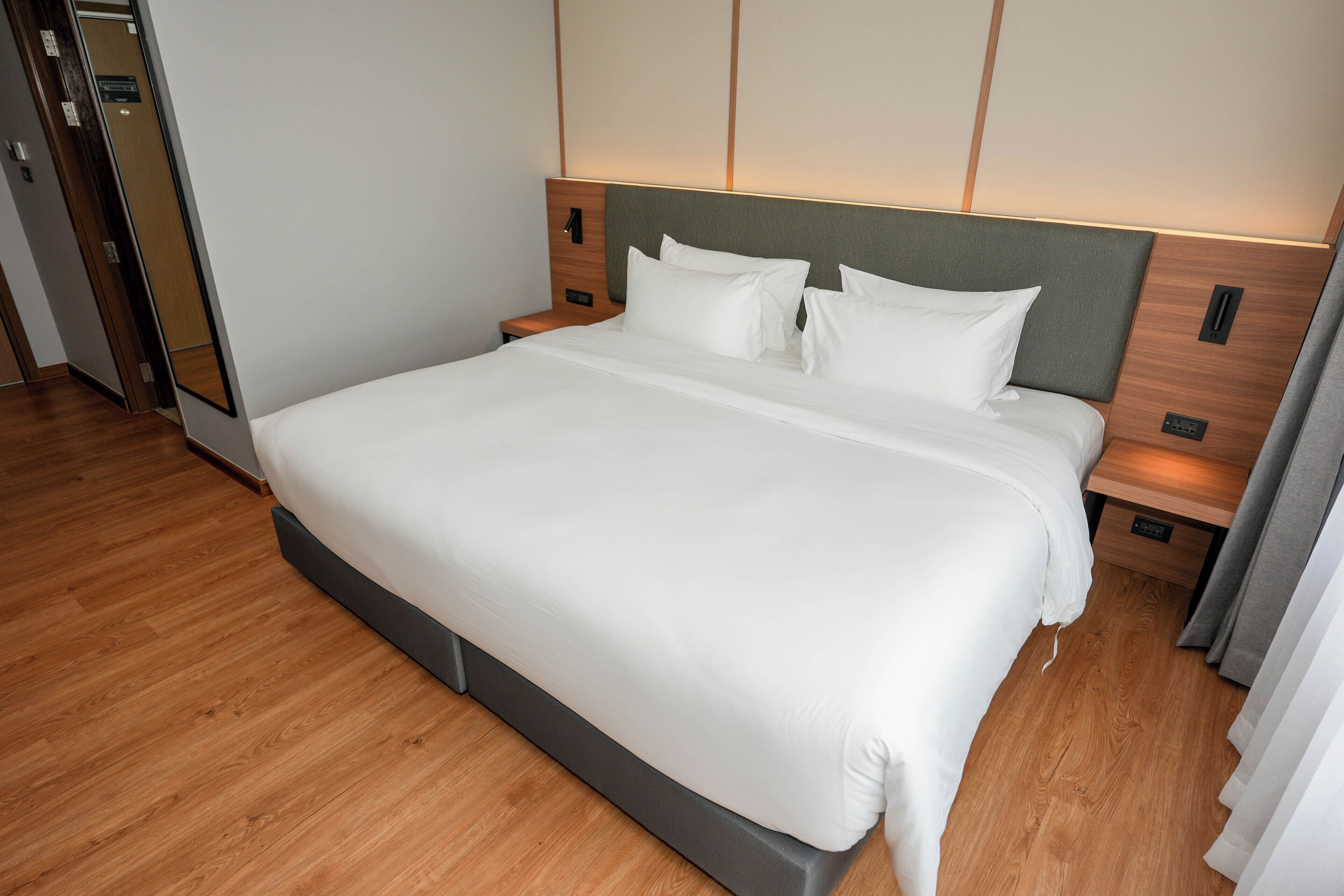 Een moderne hotelkamer met een groot bed, houten vloer en een hoofdbord met ingebouwde verlichting.