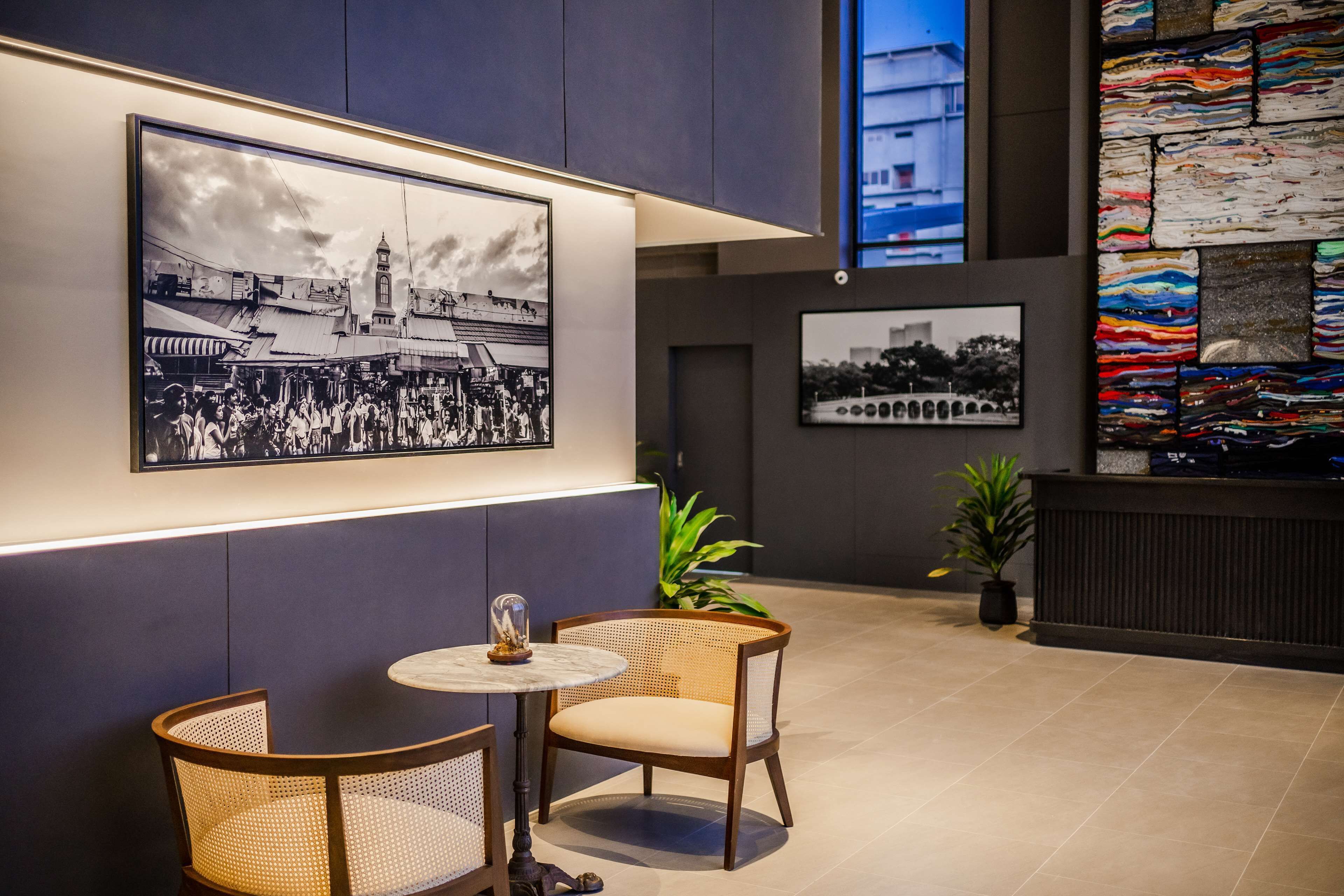 A modern interior with a round table and two wicker chairs, a framed black and white photograph on the wall, and a colorful textile artwork.