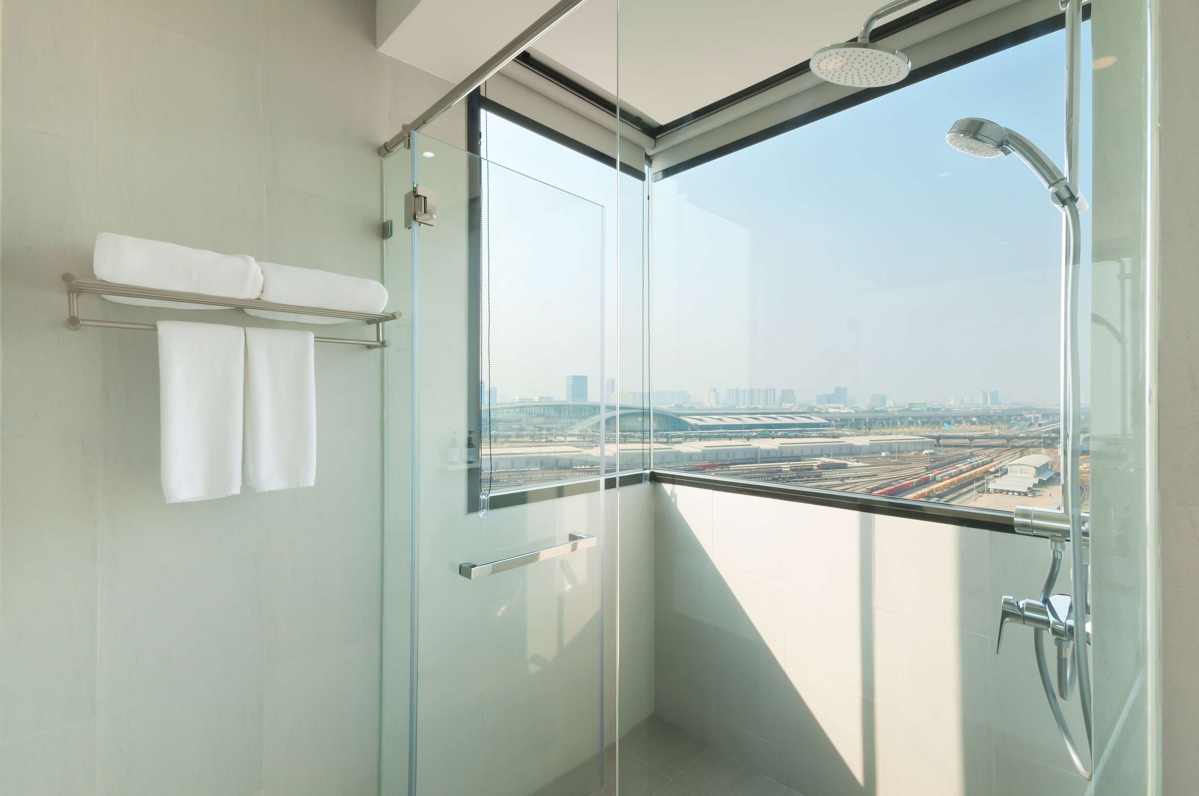 A modern bathroom with a glass shower enclosure, a towel rack, and a view of a cityscape through a large window.
